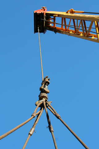 Industrial crane boom hoisting up a suspended load by cables